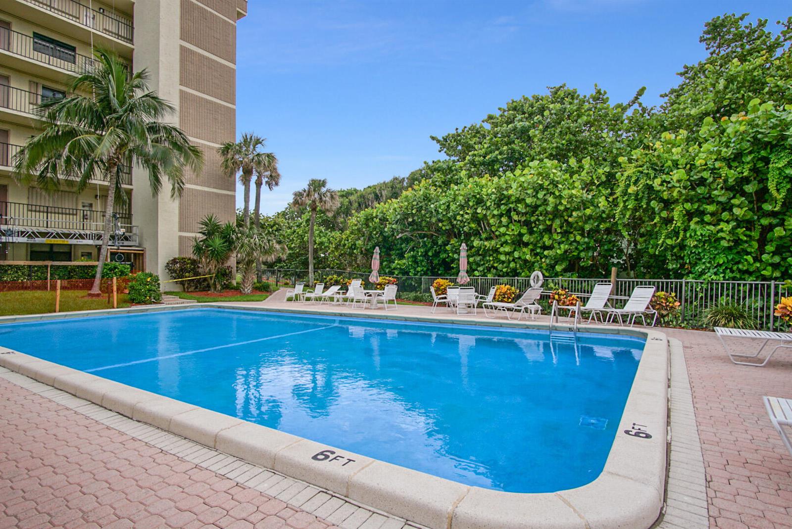 A rectangular swimming pool sits on a brick patio next to a multi-story apartment building — 10310 S Ocean Drive # 405, Jensen Beach FL 34957, JENSEN BEACH, FL