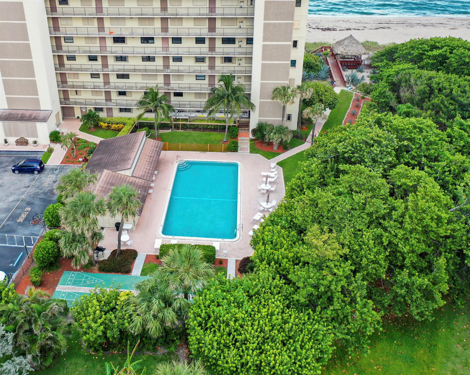 An aerial view shows a swimming pool, shuffleboard court, and multi-story building near the beach — 10310 S Ocean Drive # 405, Jensen Beach FL 34957, JENSEN BEACH, FL