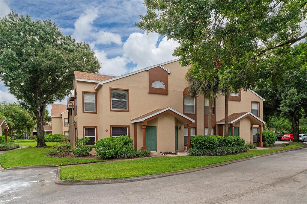 A two-story tan apartment building with green doors and brown trim under a cloudy sky — 5424 E MICHIGAN STREET UNIT 7, ORLANDO, FL