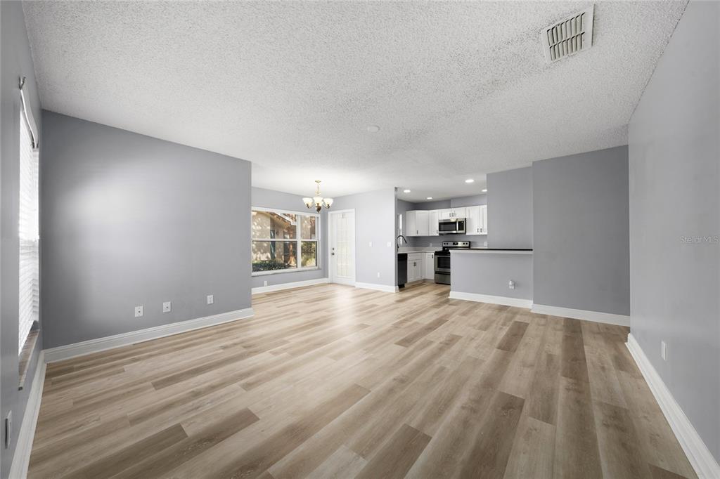 An open-concept living and dining area features light gray walls and wood-look laminate flooring — 5424 E MICHIGAN STREET UNIT 7, ORLANDO, FL