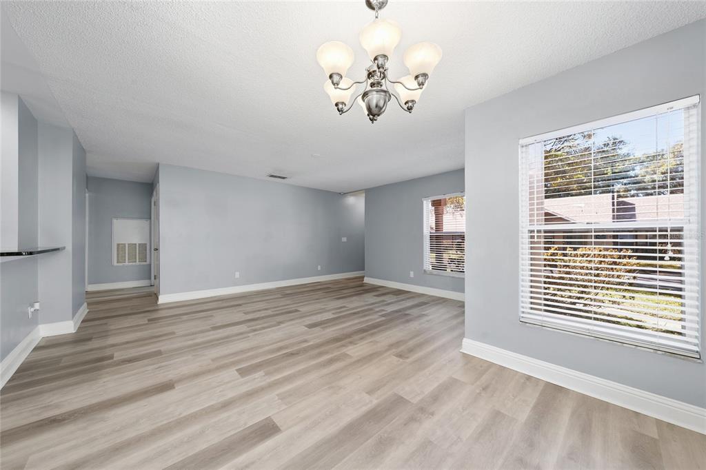 An empty room with light gray walls, wood-look flooring, a chandelier, and two windows — 5424 E MICHIGAN STREET UNIT 7, ORLANDO, FL