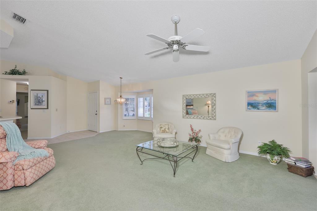 A living room with green carpet, a ceiling fan, two white chairs, and a glass table — 2429 NEW HAVEN CIRCLE, SUN CITY CENTER, FL