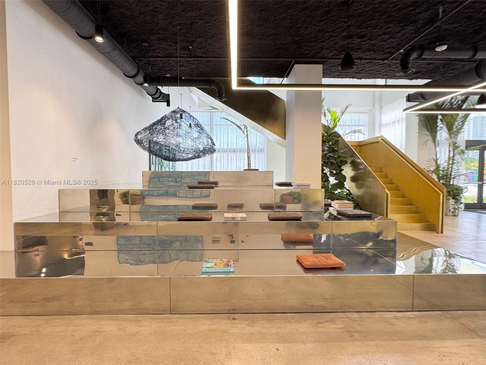 A modern interior features a tiered, mirrored display platform, a gold staircase, and industrial ceilings — 1642 NE 1st Ave # 2303, Miami FL 33132, MIAMI, FL