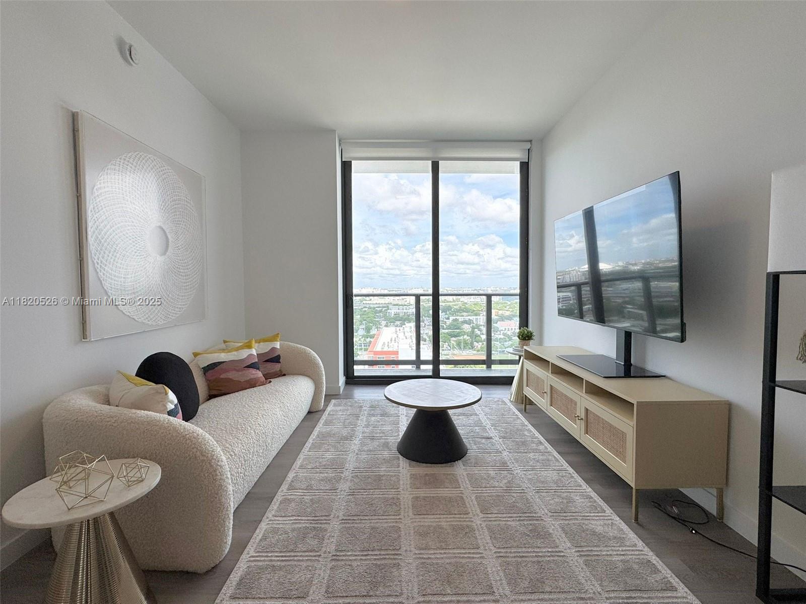 A modern living room features a textured sofa, a round coffee table, and a television — 1642 NE 1st Ave # 2303, Miami FL 33132, MIAMI, FL