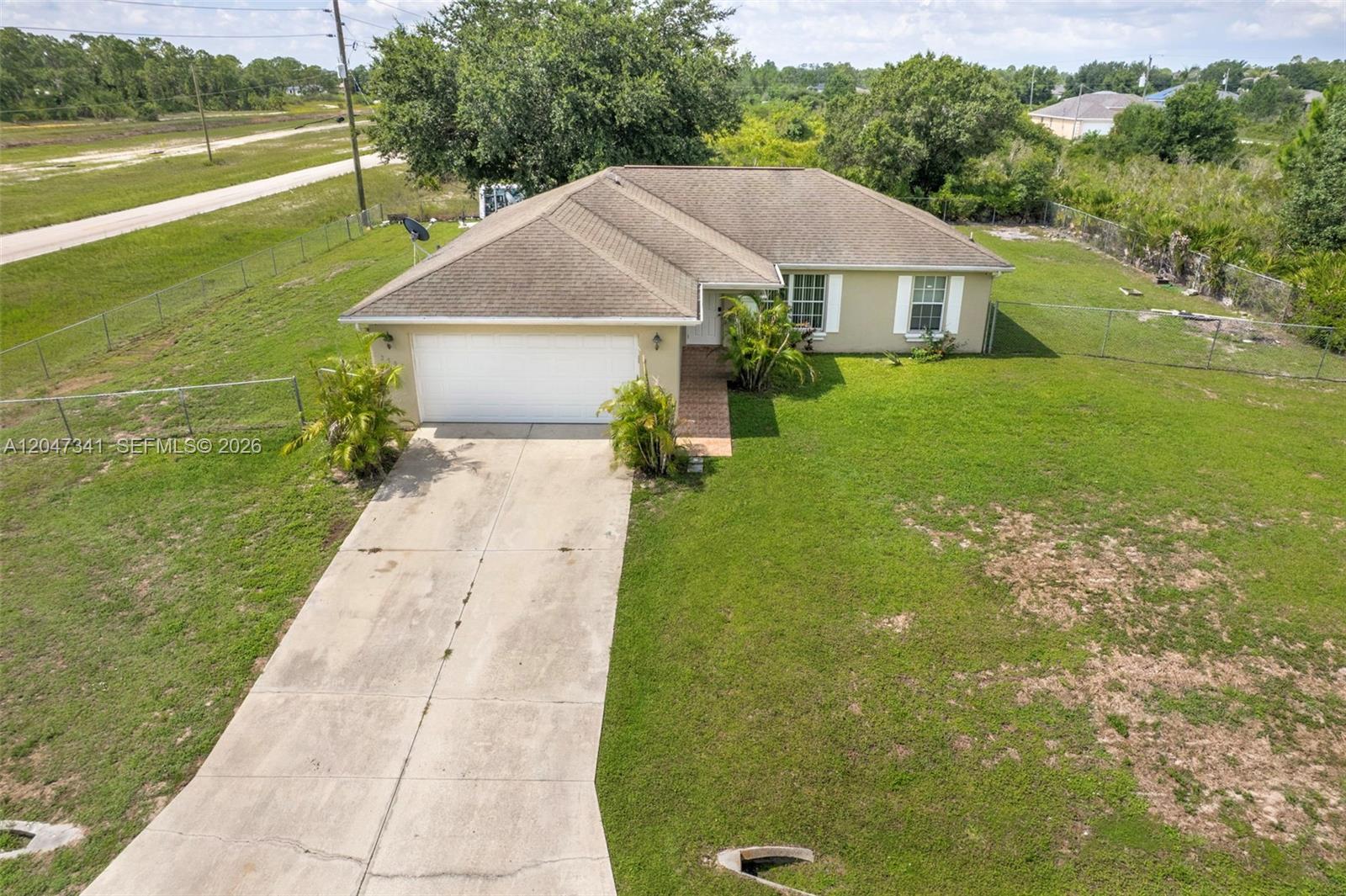 An aerial view shows a single-story house with a concrete driveway and a fenced yard — 2501 57th Street West, Lehigh Acres FL 33971, LEHIGH ACRES, FL