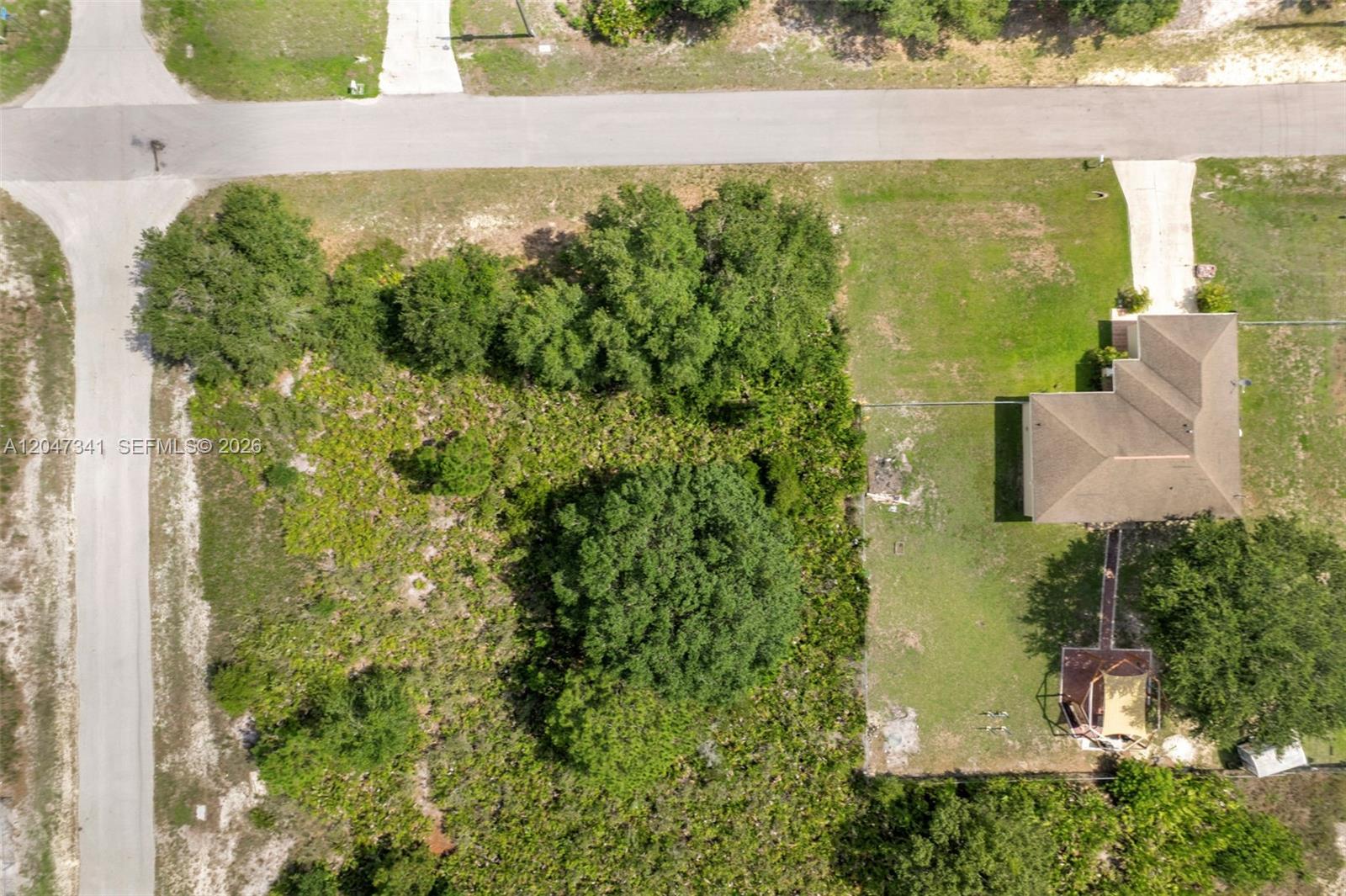 An aerial view shows a vacant, wooded lot next to a house with a driveway — 2501 57th Street West, Lehigh Acres FL 33971, LEHIGH ACRES, FL