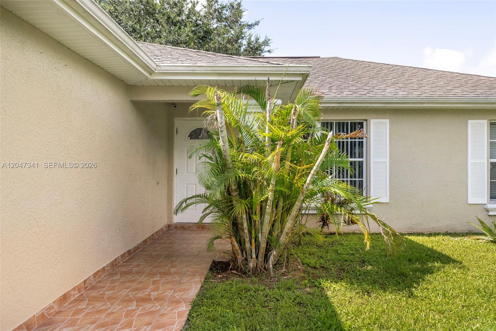 A palm tree stands in front of a house entrance with a tiled walkway — 2501 57th Street West, Lehigh Acres FL 33971, LEHIGH ACRES, FL
