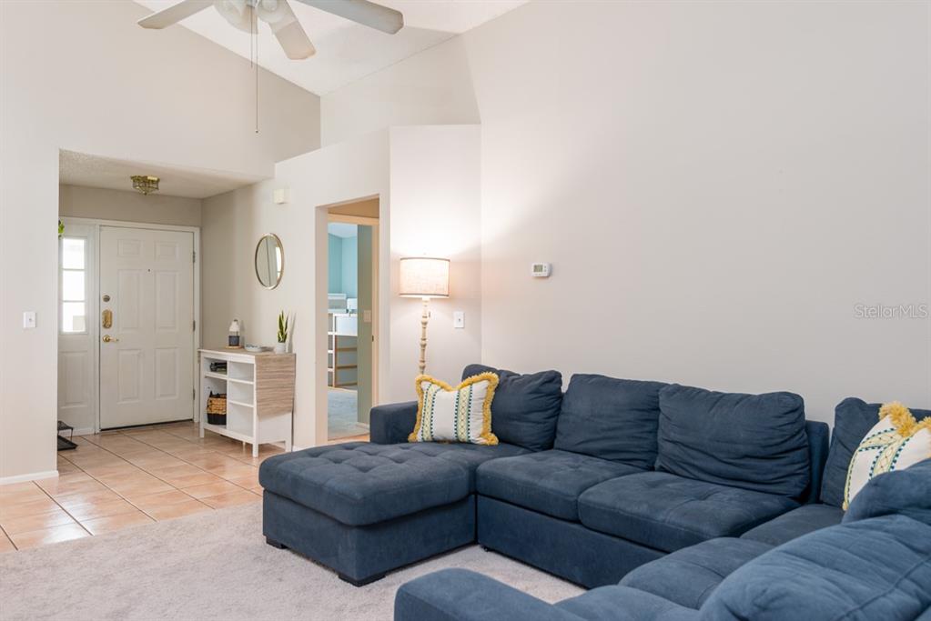 A living room features a blue sectional sofa, a vaulted ceiling, and a tiled entryway — 5917 TAYWOOD DRIVE, TAMPA, FL
