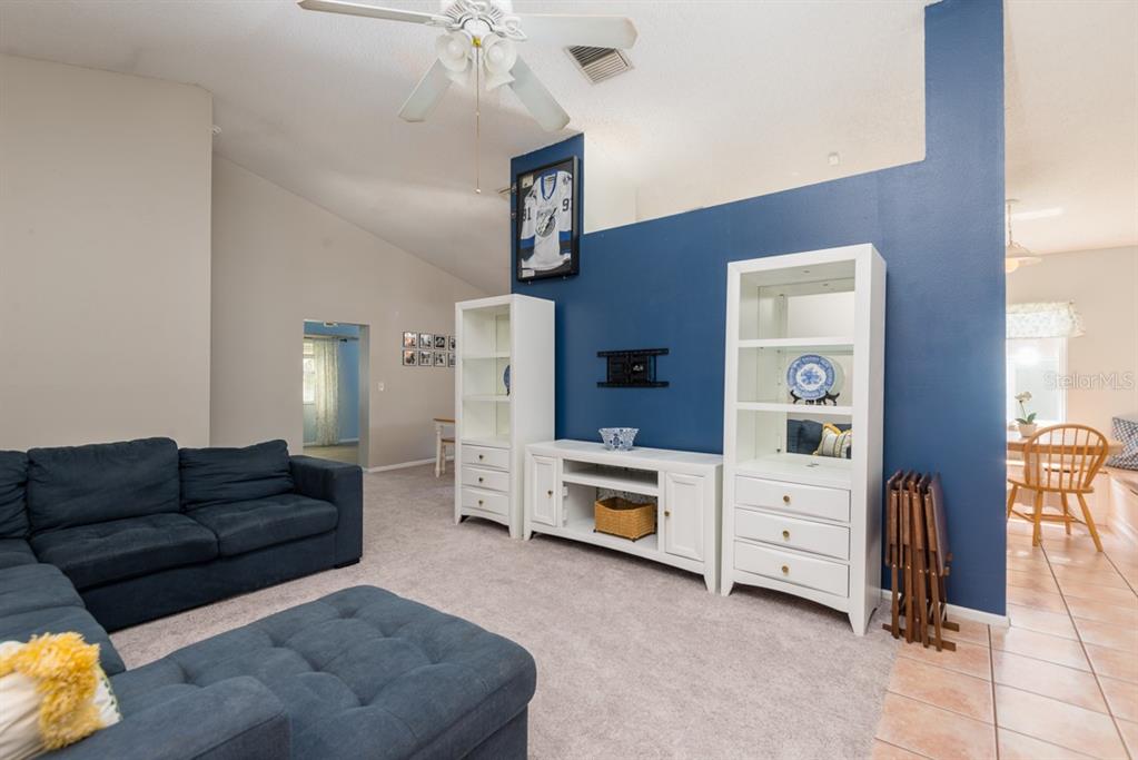 A living room features a blue accent wall, white shelving, and a dark blue sectional sofa — 5917 TAYWOOD DRIVE, TAMPA, FL