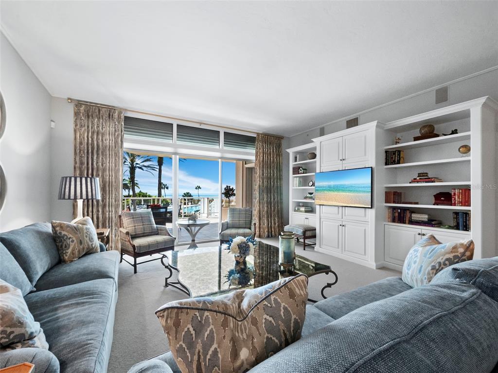 A living room features blue sofas, a glass coffee table, and built-in shelving facing a balcony — 2185 GULF OF MEXICO DRIVE UNIT 212, LONGBOAT KEY, FL