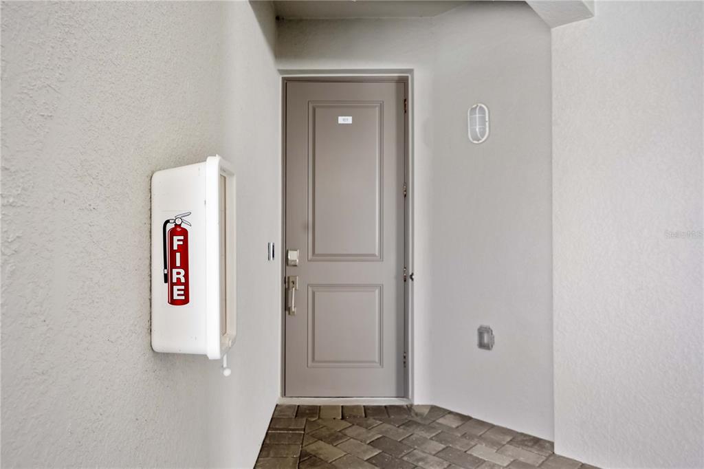 A gray door is centered in a white entryway with a fire extinguisher cabinet nearby — 12140 WELLEN GOLF STREET UNIT 101, VENICE, FL