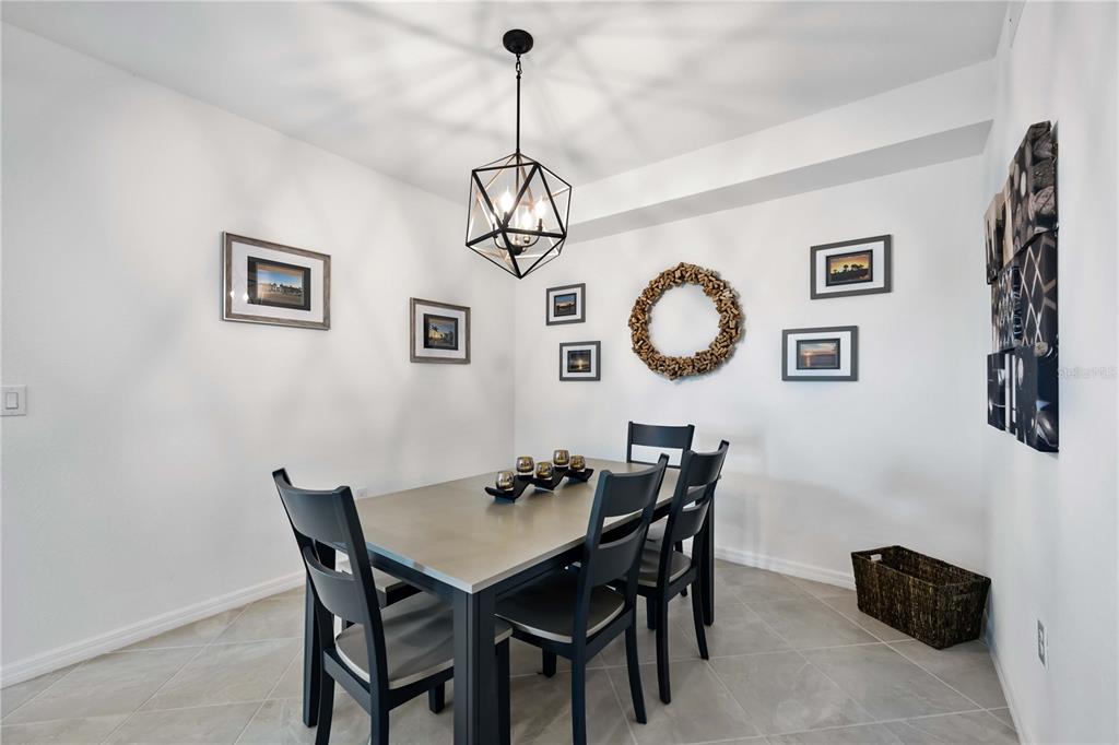A dining room features a gray table, black chairs, a geometric pendant light, and wall art — 12140 WELLEN GOLF STREET UNIT 101, VENICE, FL