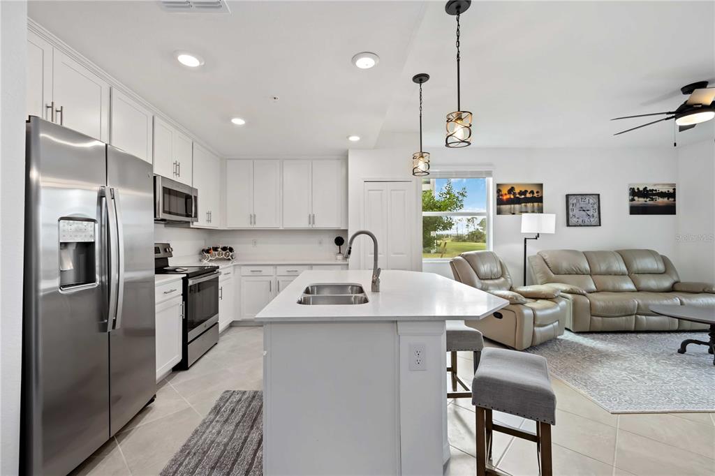 A modern kitchen with white cabinetry and a central island opens into a living area — 12140 WELLEN GOLF STREET UNIT 101, VENICE, FL