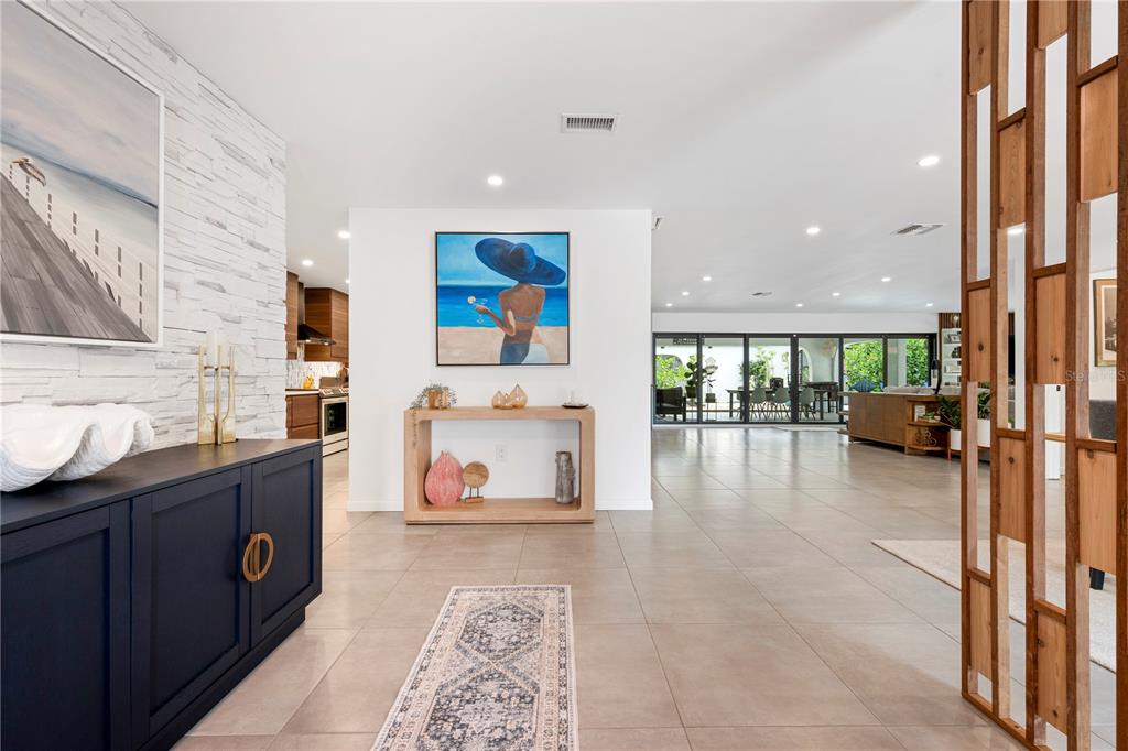 A bright, open-concept living area features tiled floors, a wooden room divider, and modern artwork — 403 51ST STREET NW, BRADENTON, FL