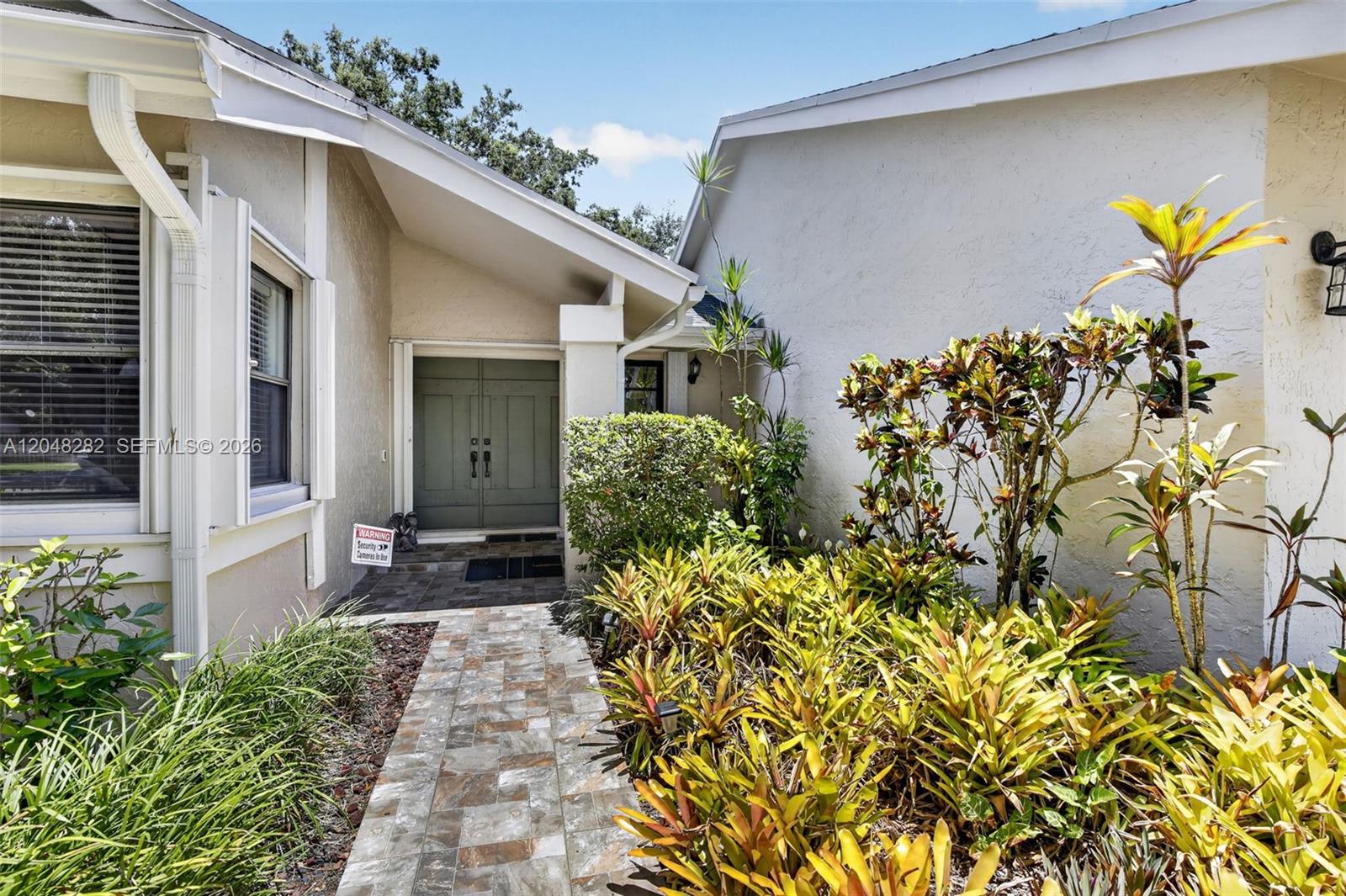 A stone walkway leads to the double front doors of a house with light-colored stucco — 12104 Landing Way, Cooper City FL 33026, COOPER CITY, FL