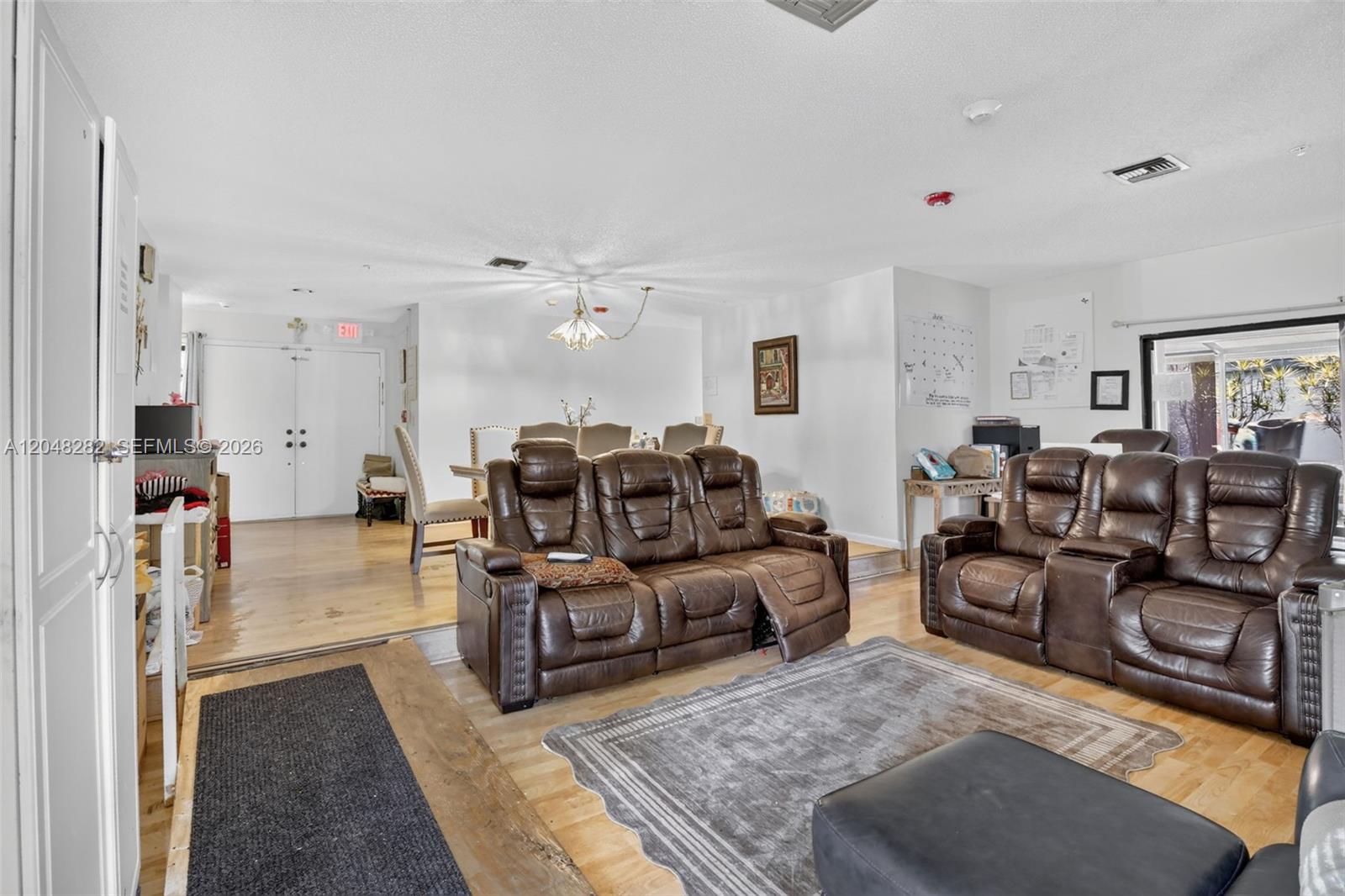 A living room features brown leather reclining sofas, hardwood floors, and an adjacent dining area — 12104 Landing Way, Cooper City FL 33026, COOPER CITY, FL