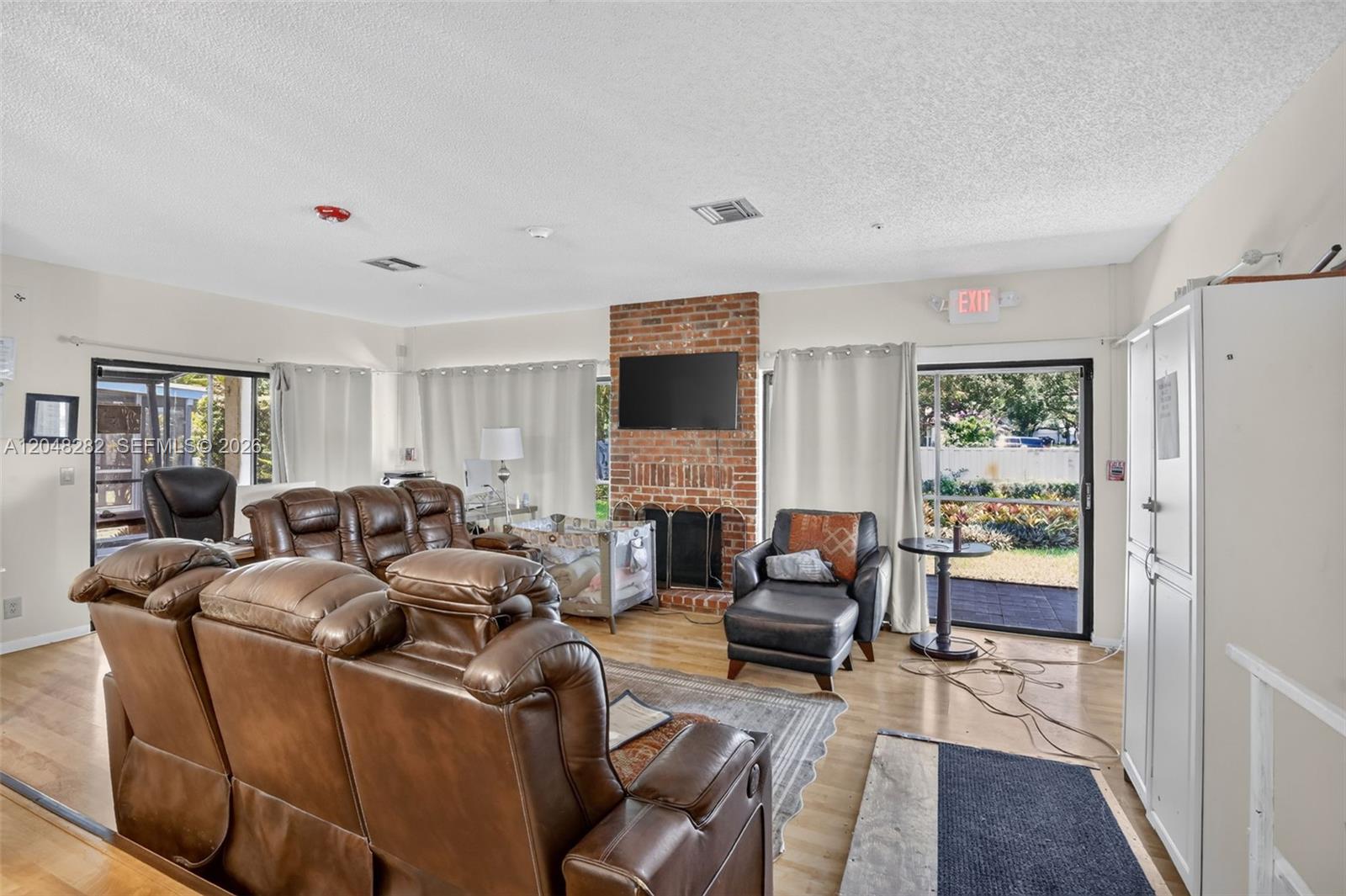 A living room features a brick fireplace, leather furniture, and a sliding glass door — 12104 Landing Way, Cooper City FL 33026, COOPER CITY, FL