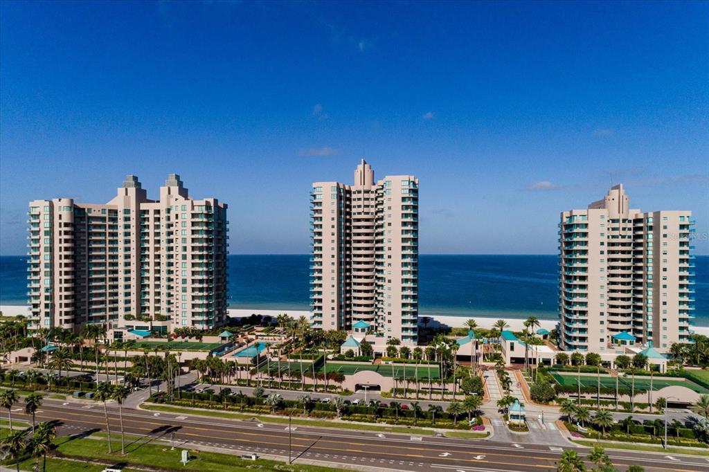 Three tall residential buildings stand along a sandy beach next to a coastal road — 1560 GULF BOULEVARD UNIT 1101, CLEARWATER BEACH, FL