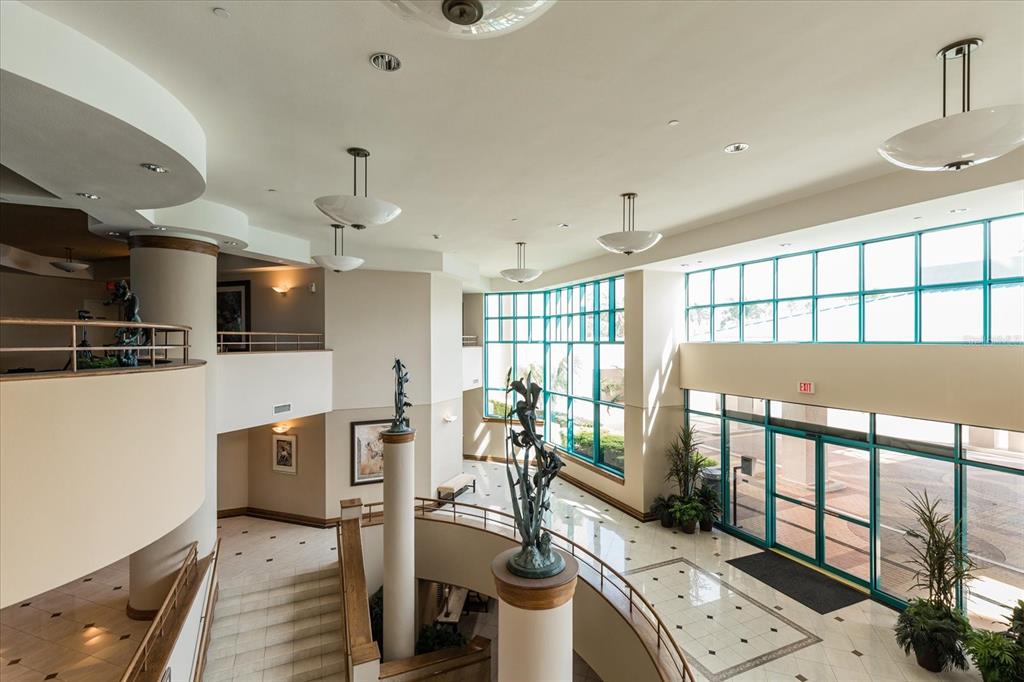 A multi-level lobby features a curved staircase, tile flooring, large windows, and a bronze sculpture — 1560 GULF BOULEVARD UNIT 1101, CLEARWATER BEACH, FL
