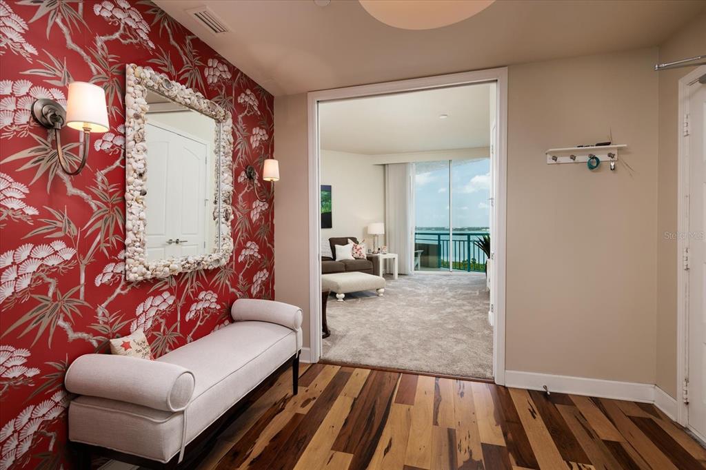 An entryway with red patterned wallpaper, a shell-framed mirror, and a bench leads to a living area — 1560 GULF BOULEVARD UNIT 1101, CLEARWATER BEACH, FL