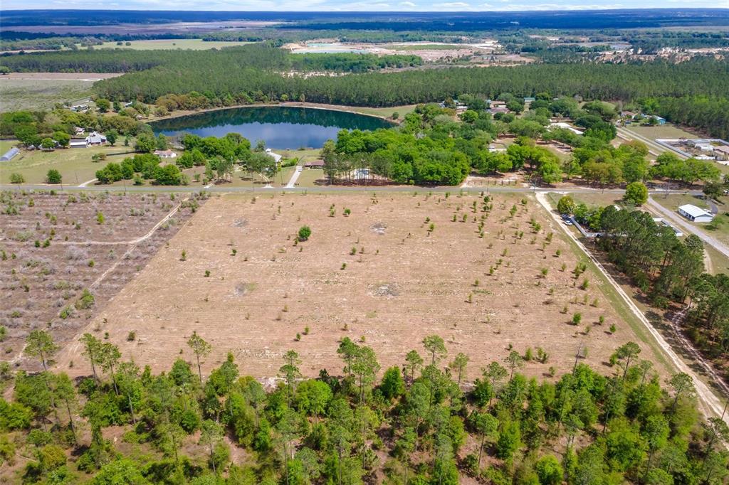 An aerial view shows a large, cleared rectangular lot adjacent to a lake and forest — SE 170TH AVENUE, WEIRSDALE, FL