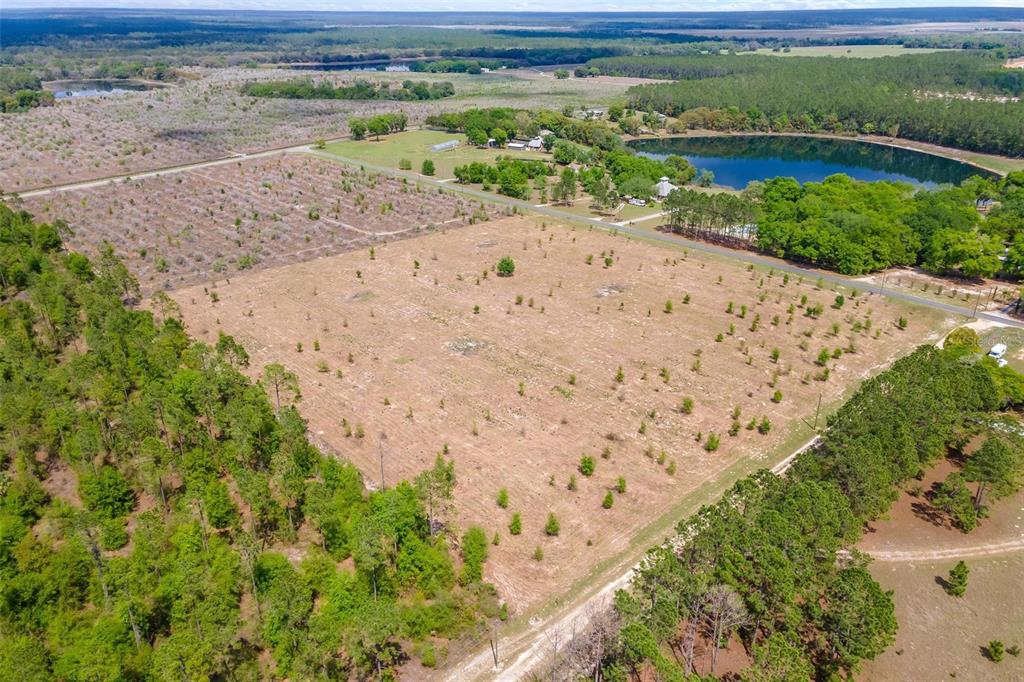 An aerial view shows a large, cleared rectangular lot surrounded by trees and a lake — SE 170TH AVENUE, WEIRSDALE, FL