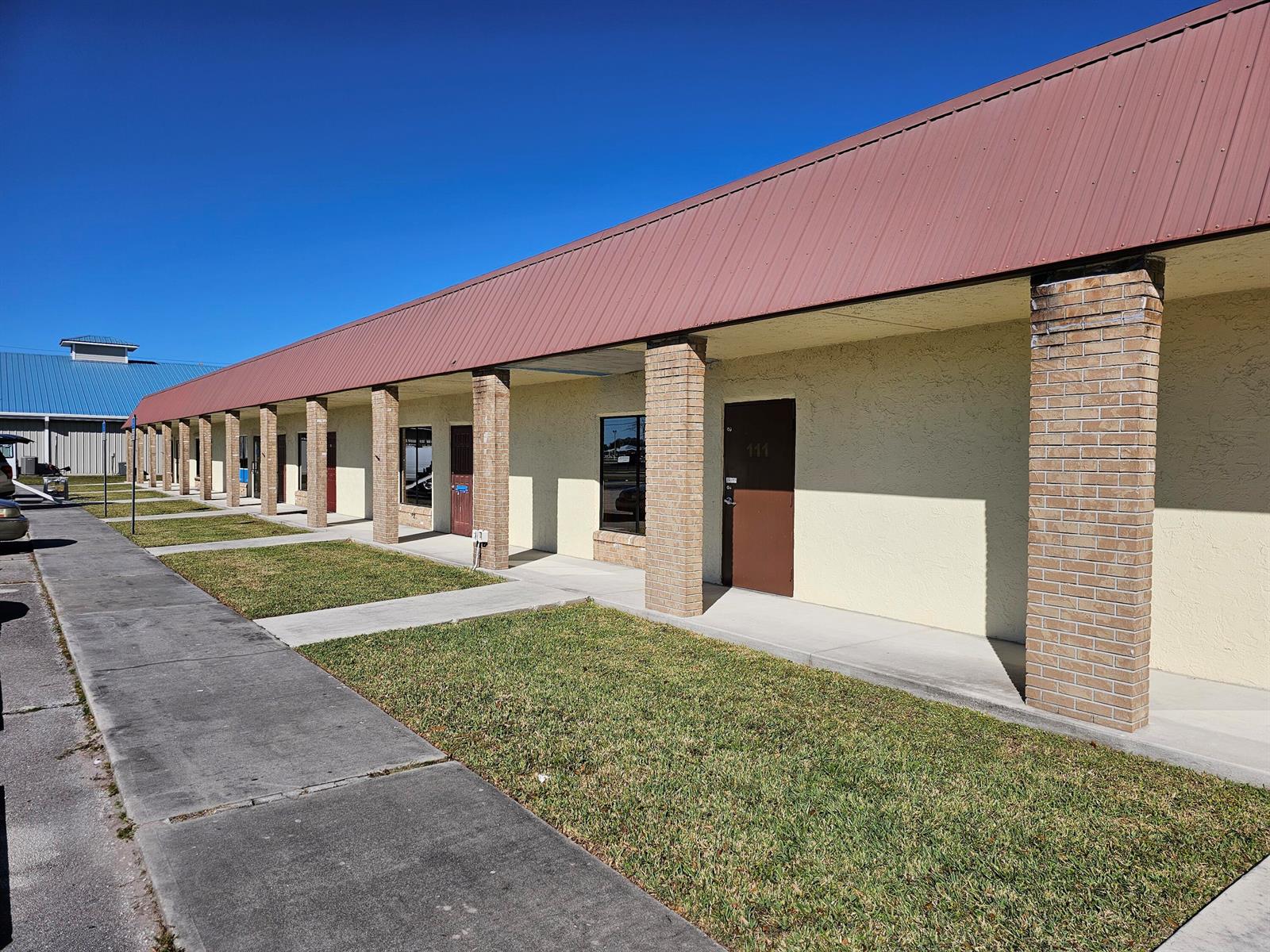 A single-story commercial building with a red metal roof and brick-columned exterior walkway — 111 NE 19th Drive, Okeechobee FL 34972, OKEECHOBEE, FL