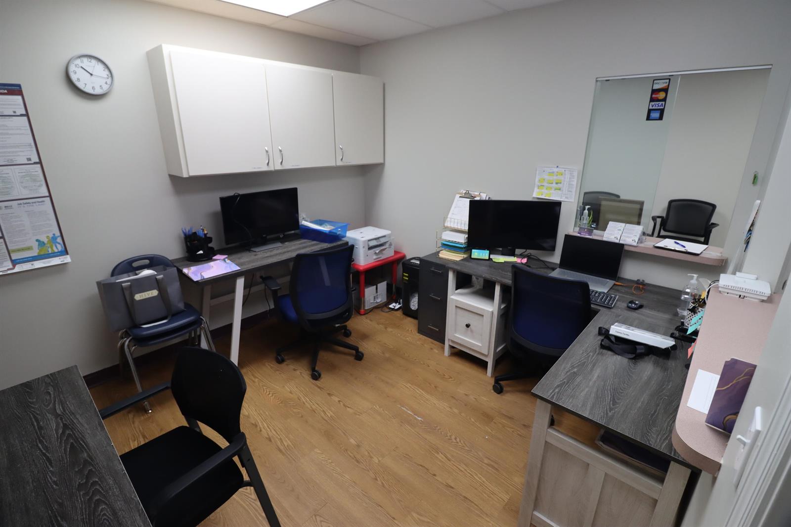 An office room features two desks with computers, blue chairs, wall cabinets, and wood flooring — 111 NE 19th Drive, Okeechobee FL 34972, OKEECHOBEE, FL
