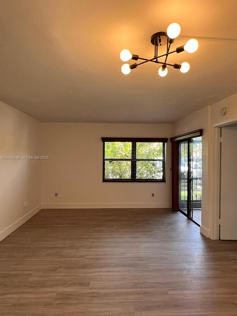 An empty room features light wood-look flooring, a modern chandelier, and a sliding glass door — 6455 W 27th Ave # 44, Hialeah FL 33016, HIALEAH, FL