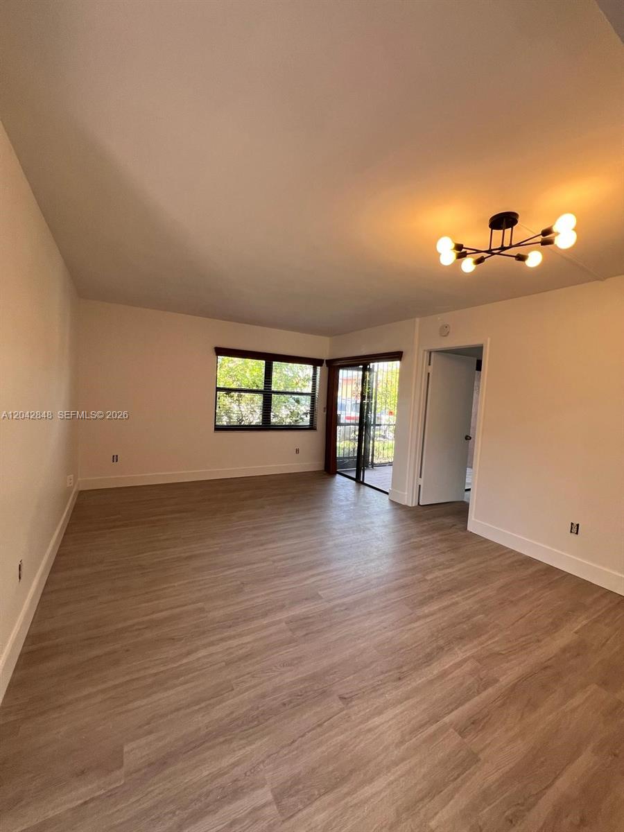 An empty room features light wood-look flooring, a modern light fixture, and a sliding glass door — 6455 W 27th Ave # 44, Hialeah FL 33016, HIALEAH, FL