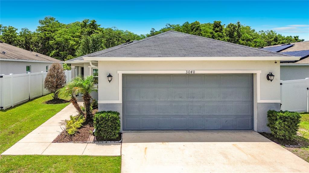 A single-story house exterior features a gray two-car garage, a concrete driveway, and white fencing — 3040 LAKES CREST AVENUE, ST CLOUD, FL