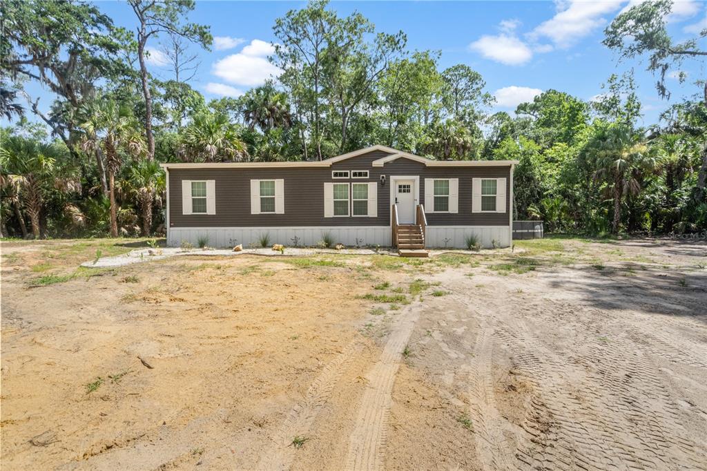 A single-story manufactured home with dark siding sits on a sandy lot surrounded by trees — 375 SAPP STREET, INGLIS, FL