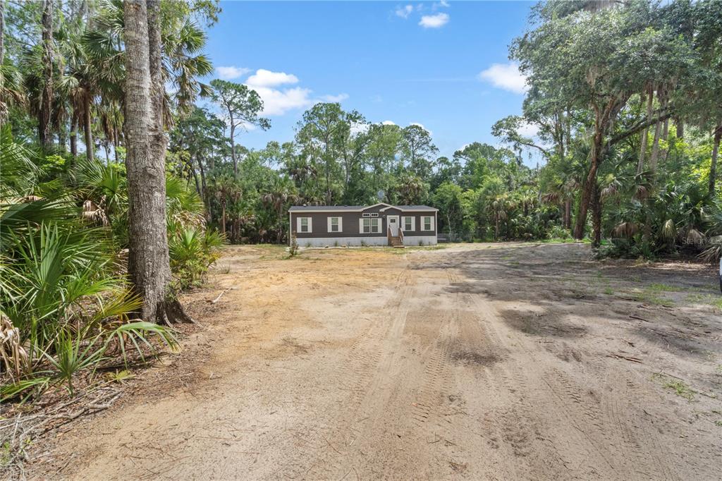 A single-story manufactured home sits at the end of a long, sandy dirt driveway — 375 SAPP STREET, INGLIS, FL