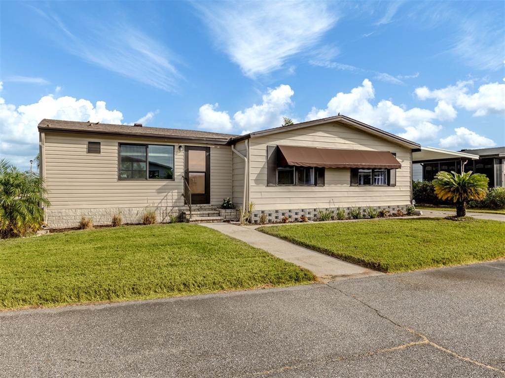 A single-story manufactured home with beige siding, a brown awning, and a front lawn — 397 CATAMARAN COURT, NORTH PORT, FL