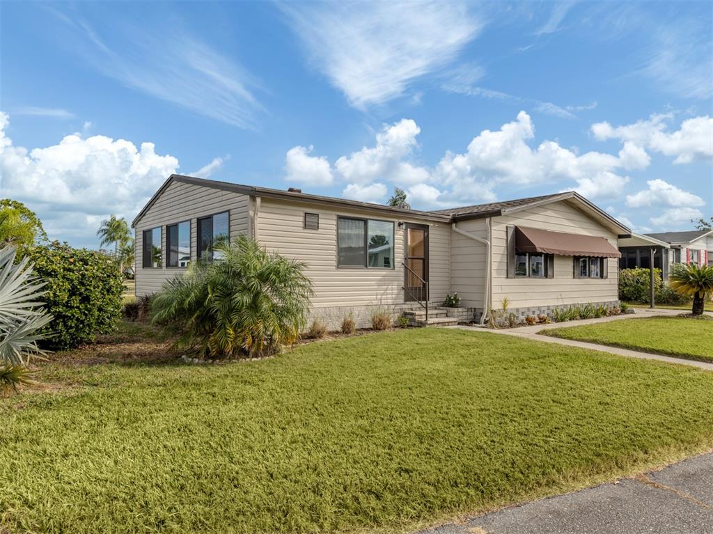 A single-story tan mobile home with a brown roof and a front lawn — 397 CATAMARAN COURT, NORTH PORT, FL