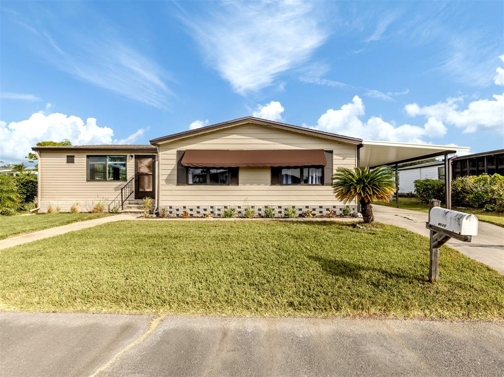 A single-story tan mobile home features a brown awning, a carport, and a front lawn — 397 CATAMARAN COURT, NORTH PORT, FL
