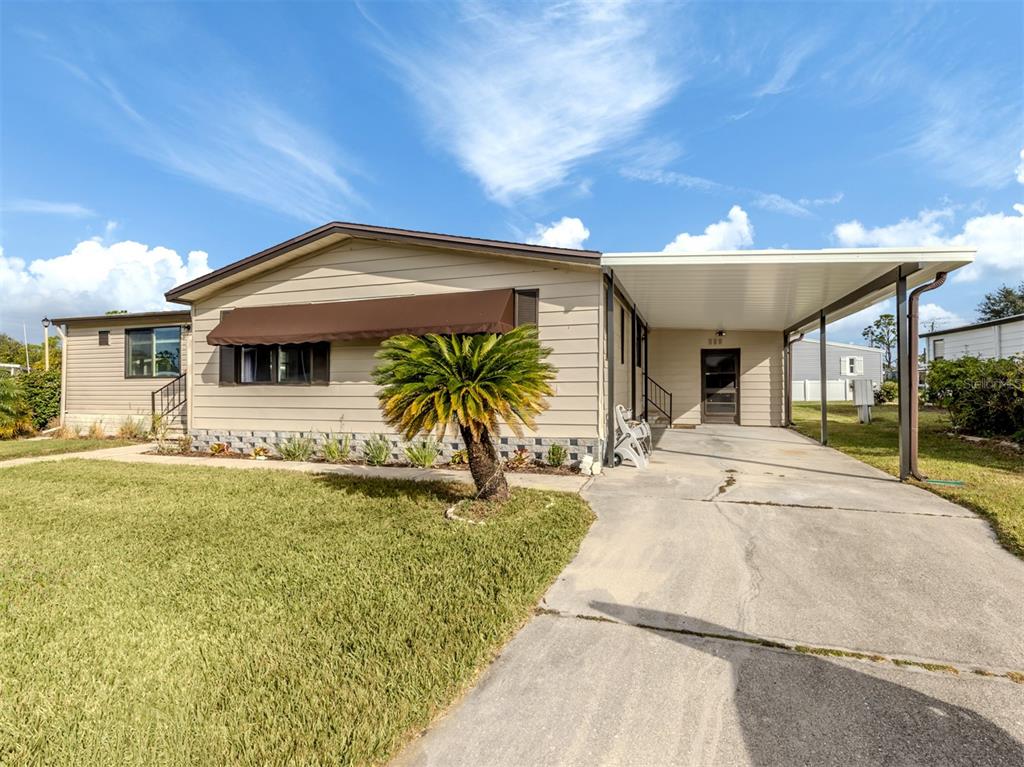 A single-story house with tan siding, a brown awning, and an attached carport — 397 CATAMARAN COURT, NORTH PORT, FL