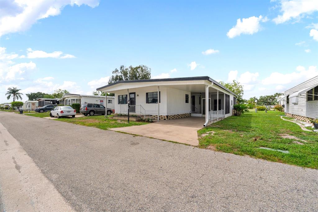 A white mobile home with a carport and driveway sits along a paved street — 6710 36TH AVENUE E UNIT 87, PALMETTO, FL