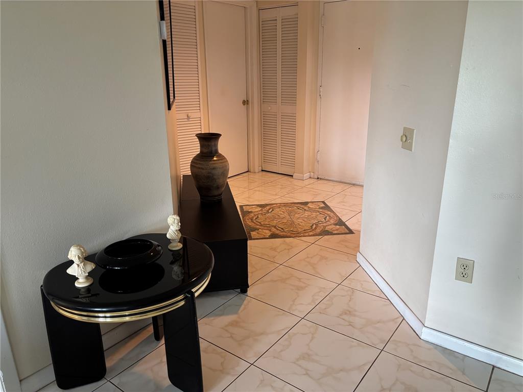 A tiled entryway features a black pedestal table, a decorative vase, and two closet doors — 2333 FEATHER SOUND DRIVE UNIT C107, CLEARWATER, FL