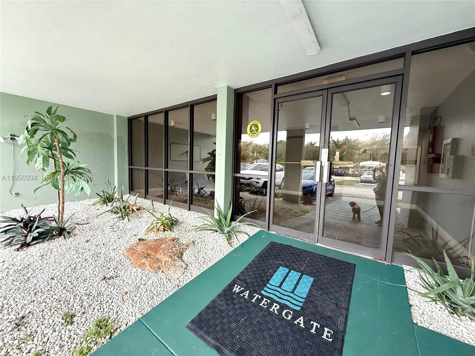The exterior entrance of a building features a gravel garden, glass doors, and a branded mat — 2771 Taft St # 411, Hollywood FL 33020, HOLLYWOOD, FL