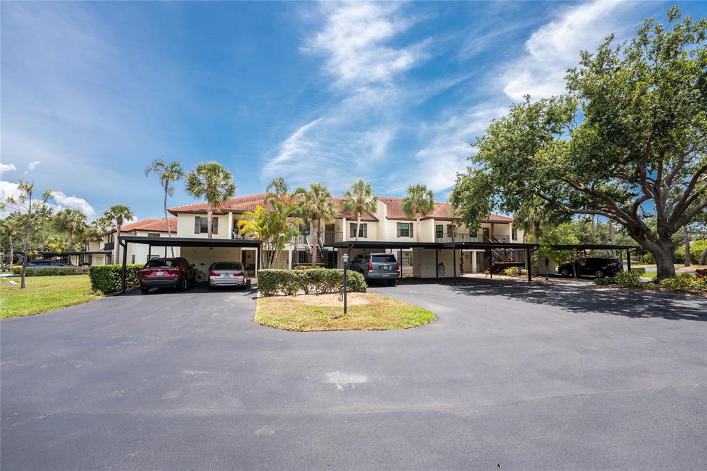 A two-story apartment building features covered parking spaces and palm trees under a blue sky — 511 PINE HOLLOW CIRCLE UNIT 511, ENGLEWOOD, FL