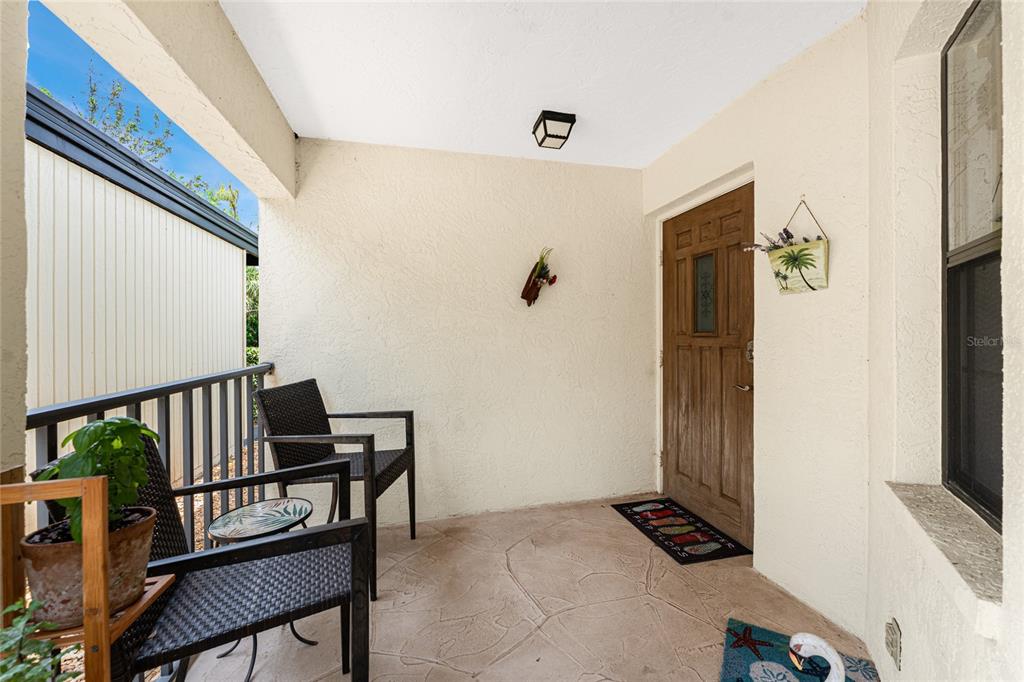 A covered front porch features a wooden door, two chairs, and a small table — 511 PINE HOLLOW CIRCLE UNIT 511, ENGLEWOOD, FL