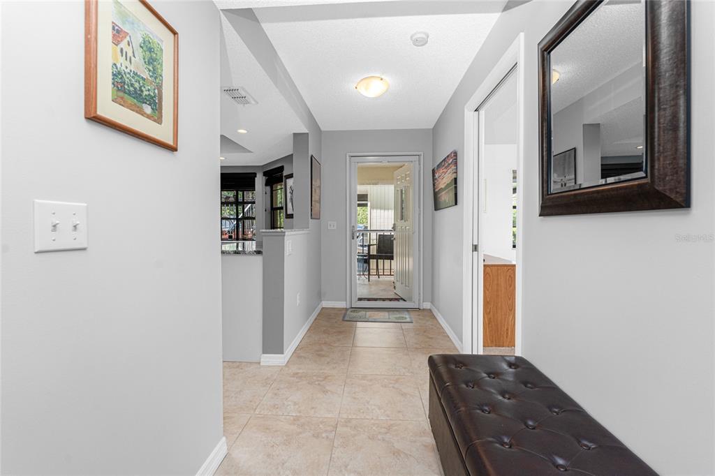A tiled hallway leads to an exterior door with a brown leather bench on the right — 511 PINE HOLLOW CIRCLE UNIT 511, ENGLEWOOD, FL