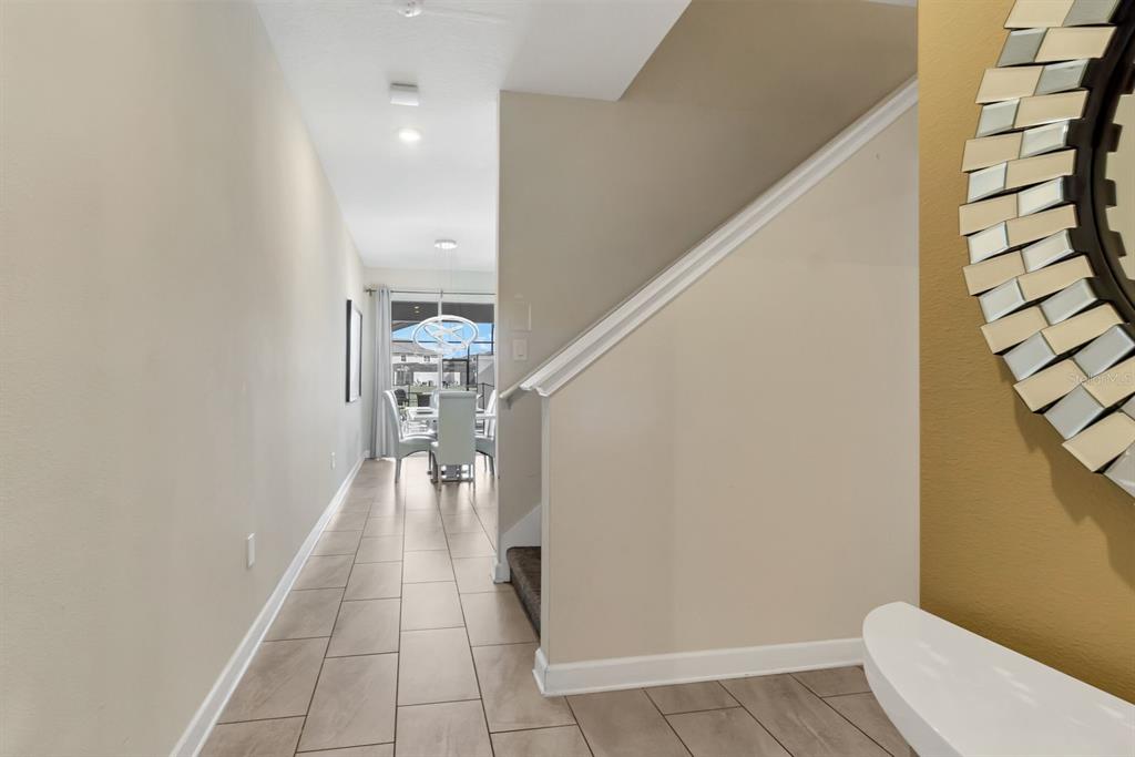 A hallway with tile flooring leads to a dining area past a staircase with railing — 4914 WINDERMERE AVENUE, KISSIMMEE, FL