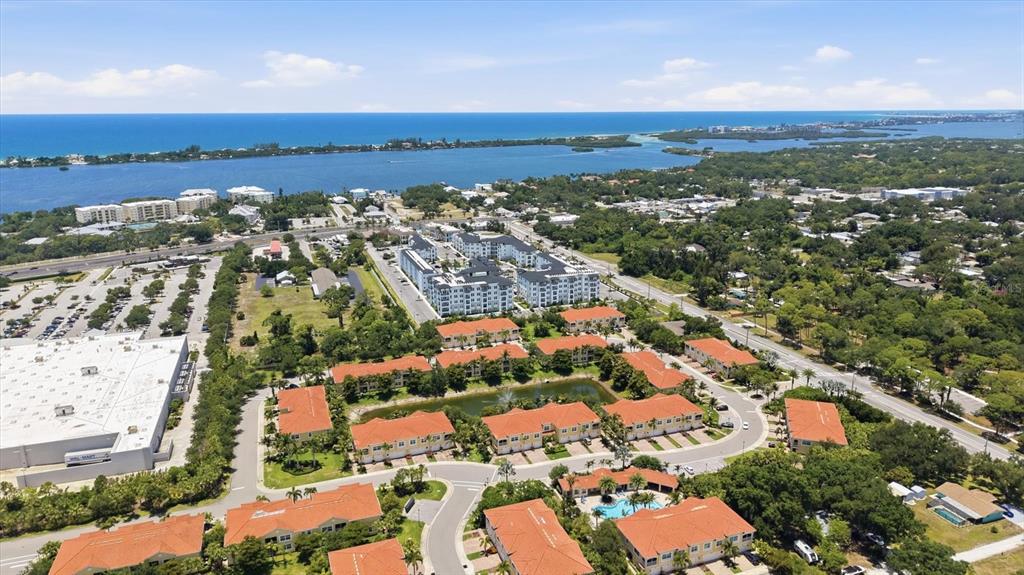 An aerial view shows a residential complex with orange-roofed buildings near a large body of water — 173 NAVIGATION CIRCLE UNIT 107, OSPREY, FL