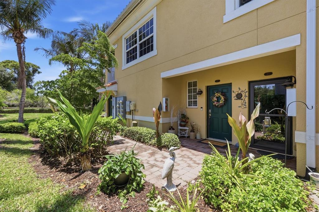 A yellow two-story townhouse exterior features a paved walkway, a dark green door, and landscaping — 173 NAVIGATION CIRCLE UNIT 107, OSPREY, FL