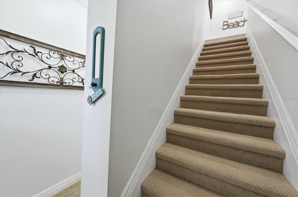 A carpeted staircase with white walls and decorative wall art leads to an upper level — 173 NAVIGATION CIRCLE UNIT 107, OSPREY, FL