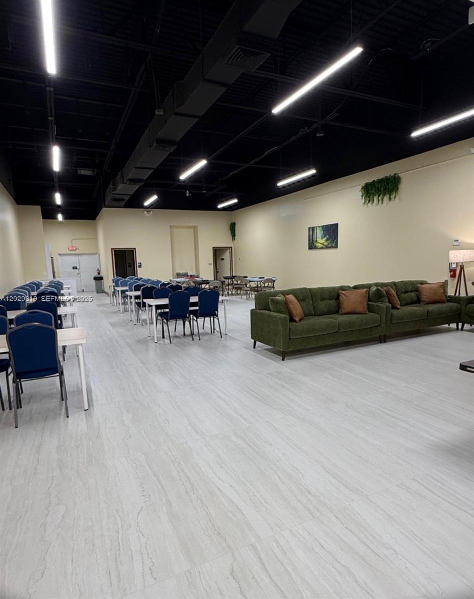 A large, open-concept room features rows of tables with blue chairs and green sofas — MIAMI, FL