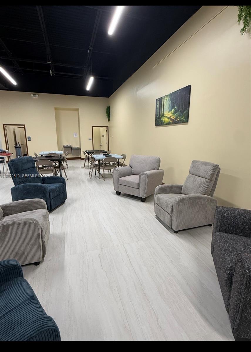 A large room features light-colored tile flooring, beige walls, and several armchairs and tables — MIAMI, FL