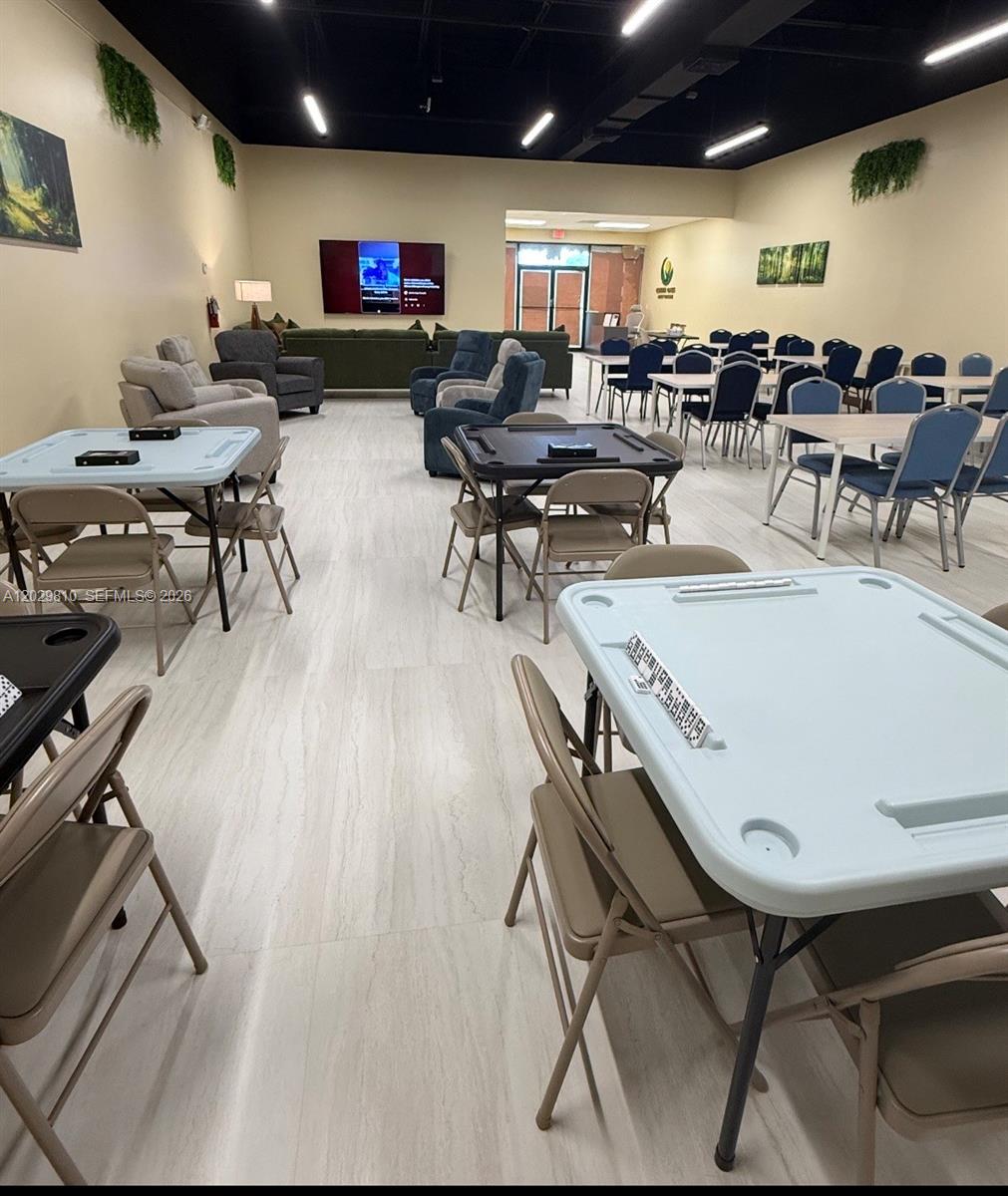 A large community room features multiple folding tables, chairs, lounge seating, and a wall-mounted television — MIAMI, FL